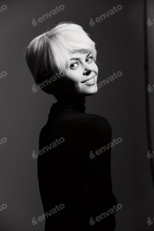 Preview: Smiling woman with short blonde hair, wearing a fitted black top, looking over her shoulder against