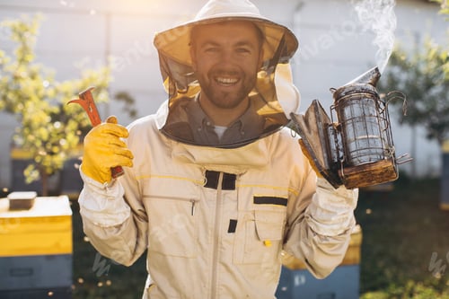 Preview: Portrait of a happy male beekeeper working in an apiary near beehives with bees. Beekeeping concept.