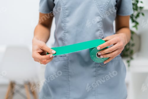 Preview: Physiotherapist holding green kinesio tape for patient therapy