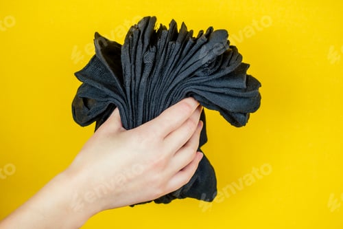 Preview: a stack of fresh new black socks in hand on a yellow background