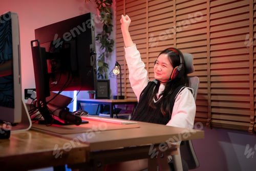Preview: Teenage girl gamer wearing headphones and playing on a desktop computer in a colorful gaming setup
