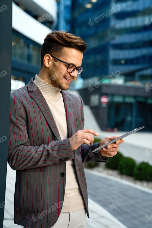 Preview: Happy young business man with tablet at work in modern urban background
