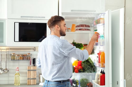 Preview: Man taking bottle with juice out of refrigerator in kitchen