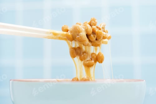 Preview: Wooden chopsticks holding japanese natto beans against background of blue tiles.