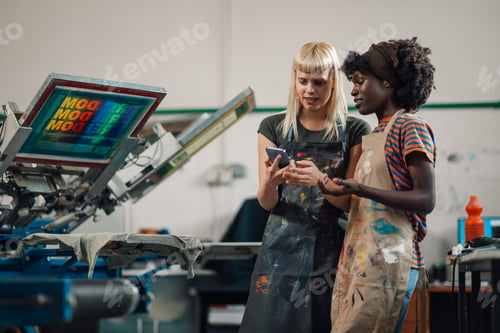 Preview: Interracial female graphic technicians at print shop looking at phone.