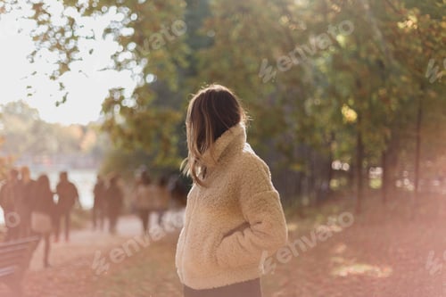 Preview: A young woman in a cosy jacket in the light of a park in autumn