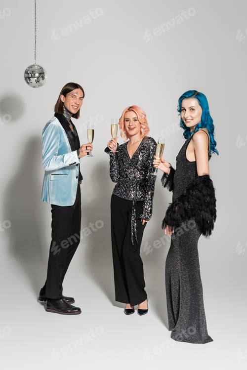 Preview: full length of elegant nonbinary people with champagne glasses celebrating christmas on grey