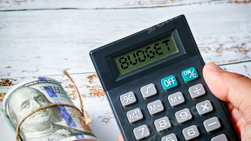 Preview: Managing Finances: Hand Holding Calculator Displaying 'BUDGET' Next to Rolled US Currency