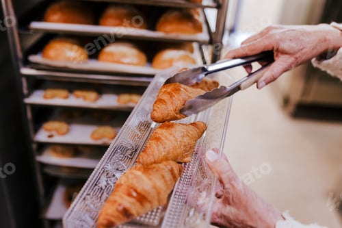 Preview: close up view of woman holding holding rack of croissants in a bakery.