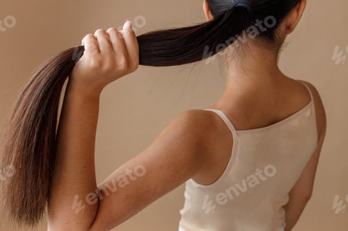 Preview: Brunette young woman holding her ponytail in studio