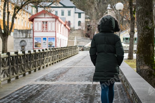 Preview: Lonely person with a coat walking along the sidewalk near tall trees