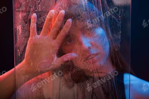 Preview: Studio shot in dark studio with neon light. Portrait of beautiful girl behind wet glass