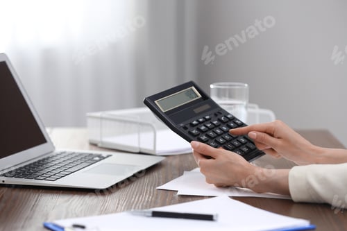 Preview: Woman using calculator at table indoors, closeup