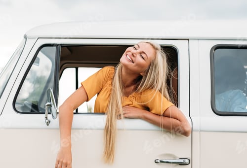 Preview: Happy blond woman with closed eyes sitting on a driver seat enjoying a road trip