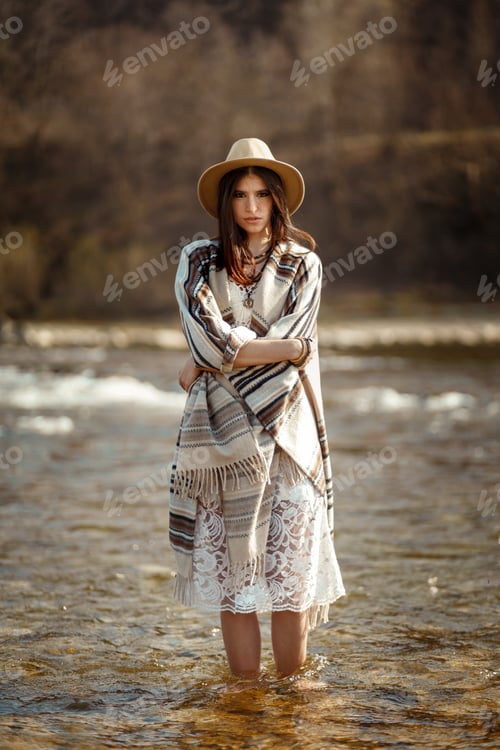 Preview: beautiful woman traveler wearing hat and poncho standing in water of river