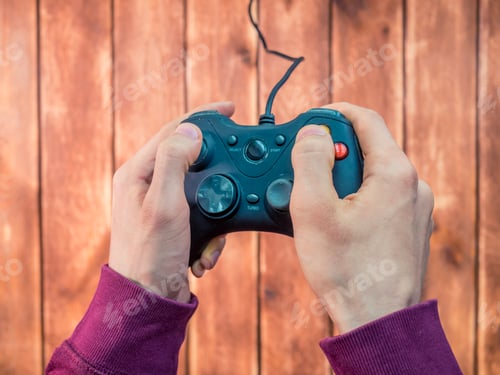 Preview: person's hands playing video game on the console using joystick on the wooden background