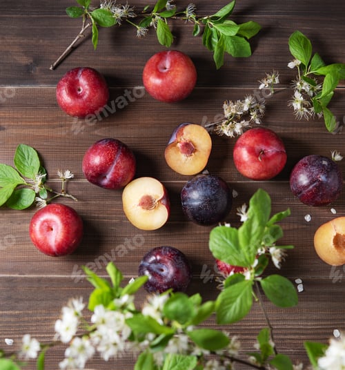 Preview: a few juicy red plums with branch blossom flowers on a brown wood background. Top view