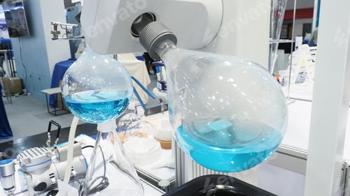 Preview: A laboratory rotary evaporator setup with large round-bottom flasks containing blue liquid.