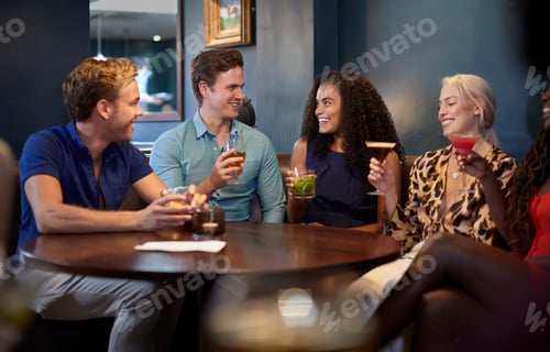 Preview: Group Of Young Friends Sitting Around Table In Bar Together On Night Out