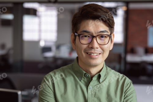 Preview: Asian man in glasses smiling confidently in modern office environment