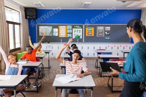 Preview: In school, students raising hands in classroom while Indian female teacher with tablet instructing