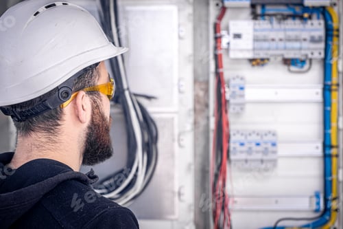 Preview: A male electrician works in a switchboard with an electrical connecting cable.