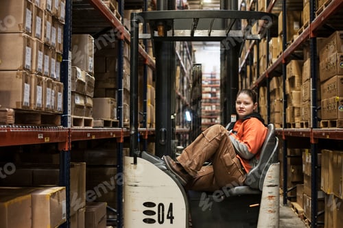 Preview: Caucasian female warehouse worker sitting in a motorized stock picker surrounded by products stored