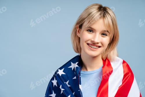 Preview: Smiling beautiful young woman with blonde hair holding American flags looking at camera, copy space