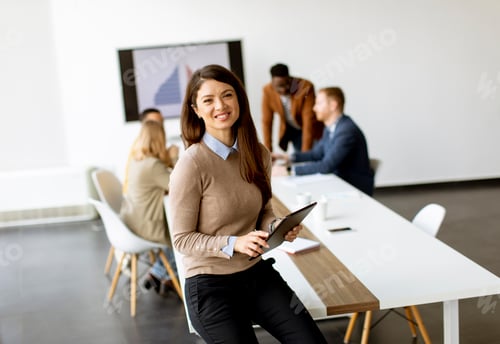 Preview: Young business woman standing in the office and using digital tablet in front of her team