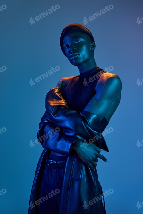 Preview: Vibrant young African American man in stylish attire poses elegantly under blue lighting