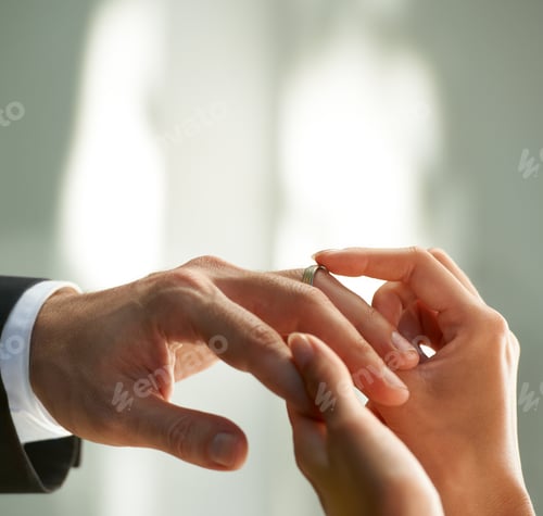 Preview: Cropped view of a bride slipping a ring on to her grooms finger
