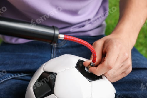 Preview: Man inflating soccer ball with manual air pump indoors, closeup