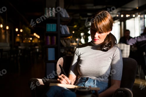 Preview: Mid adult woman writing in diary while sitting at cafe