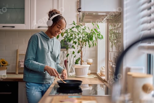 Preview: Happy black teenage girl preparing herself a meal in the kitchen.