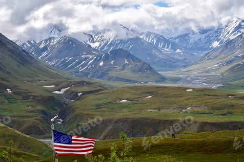Preview: American flag blowing in front of a gorgeous Alaska landscape with green hills