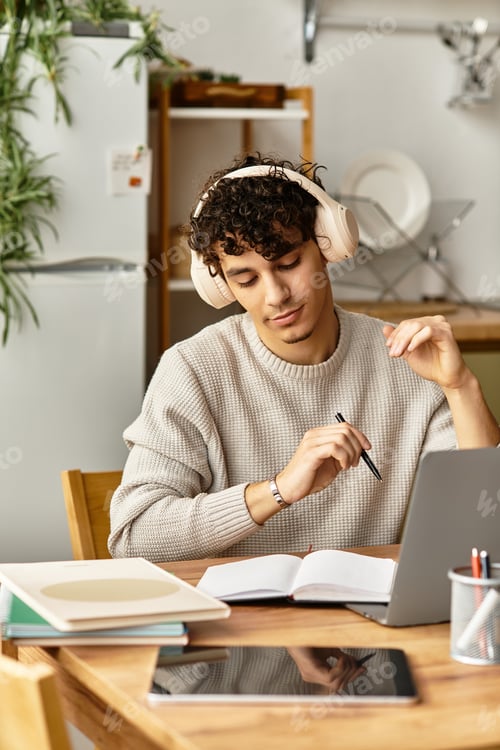 Preview: Charming young man studying intently with headphones in a cozy home environment