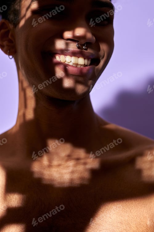 Preview: Close-up verticale portrait of smiling male in shadow. Naked torso young man on purple background