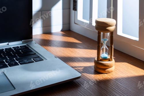 Preview: A close-up of a small hourglass next to a laptop.