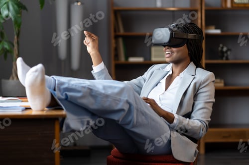 Preview: Curious afro businesswoman in vr goggles headset touching 3d virtual objects sit at office workplace