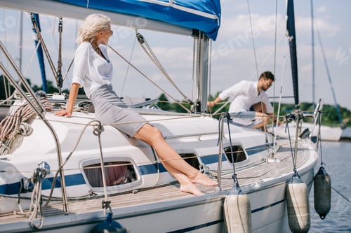 Preview: beautiful young woman sitting on yacht and looking at man behind