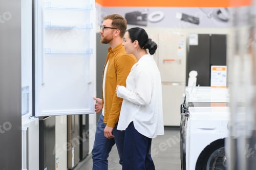 Preview: Young couple, satisfied customers choosing fridge in appliances store
