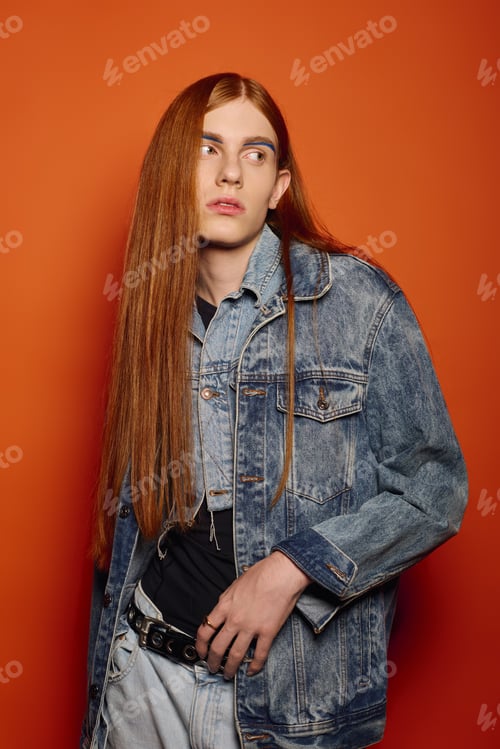 Preview: Young man with long red hair expresses deep emotions against a vibrant orange backdrop