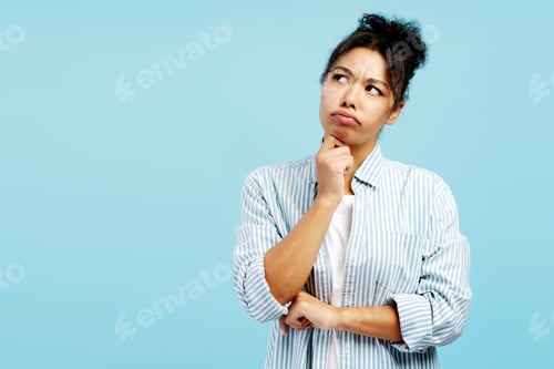 Preview: Pensive young woman reflecting with hand on chin on blue background