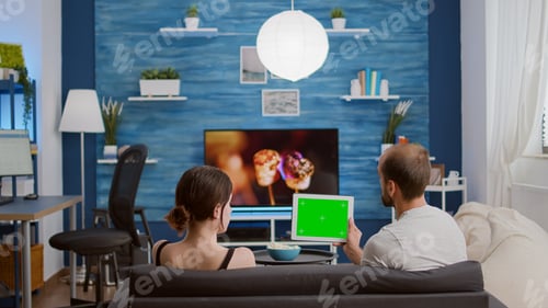 Preview: Couple on sofa watching online show using streaming app on digital tablet with green screen