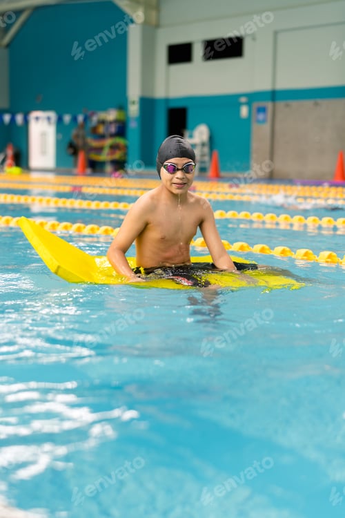 Preview: Child learning swimming using a kickboard in pool