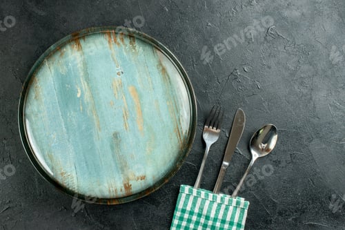 Preview: top view round plate fork knife and spoon green and white checkered napkin on dark ground with copy