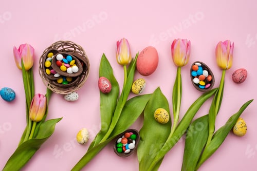 Preview: Multi-colored candy in the chocolate eggs and fresh tulips lie on a pink table.- Easter concept