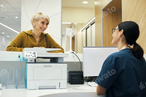 Preview: Middle Aged Woman Smiling While Speaking with Female Receptionist