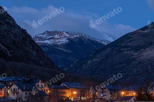 Preview: Illuminated houses under range mountains under blue sky at night in Barruera city