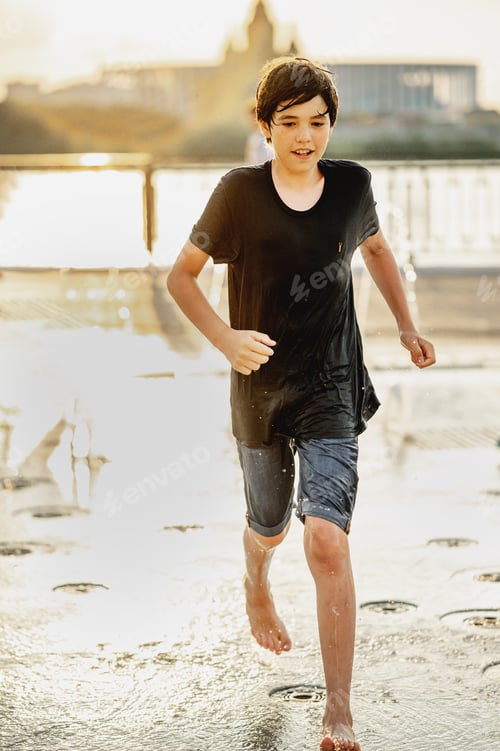 Preview: The boy runs under the splashes of the fountain on a hot summer day